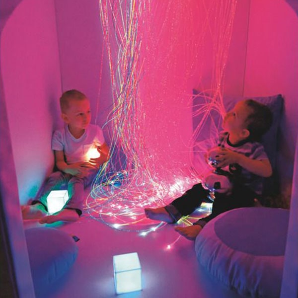 Sensory room with pink and purple wall lighting, bubble tubes, mirrors, and cloud-shaped ceiling panels.