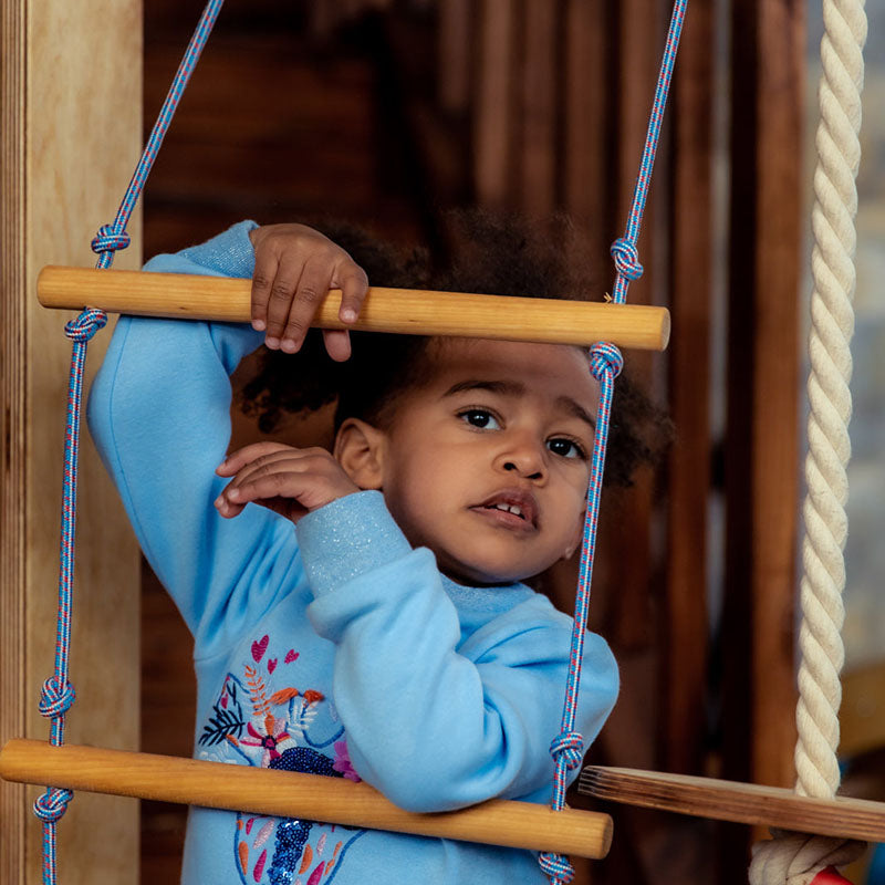 Indoor Wooden Playhouse with Triangle ladder, Slide Board and Swings with a kid playing on the rope ladder