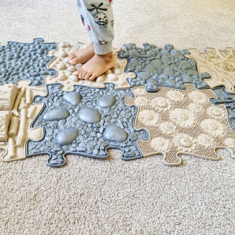 Children's play mat with various sensory textures with a kid standing on it. 