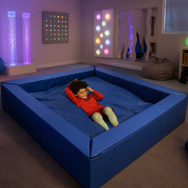 Large blue sensory crash pit in a sensory playroom with therapy equipment