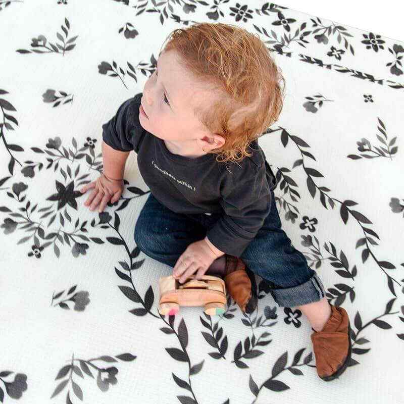 Shwally August Rose White Reversible Playmat with a toddler playing with a car