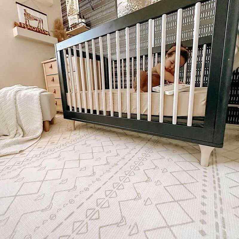 Shwally Enya Double Sided Playmat in a nursery with a baby crib sitting on it. 