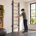 BenchK Wall Bars 200 with a teen holding a wooden rung during a standing stretch in a home exercise room