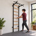 BenchK Wall Bars 221 – Teen holding a wooden rung for a supported standing stretch in a home exercise room.