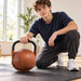 BenchK Leather Kettlebell – Teen kneeling beside the stationary brown leather kettlebell with a hand resting on its black metal handle; floor mat is sold separately.