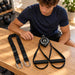BenchK Recoil S2 Trainer – Teen inspecting the trainer, two handles and lashing strap laid out before training; background exercise equipment is sold separately.