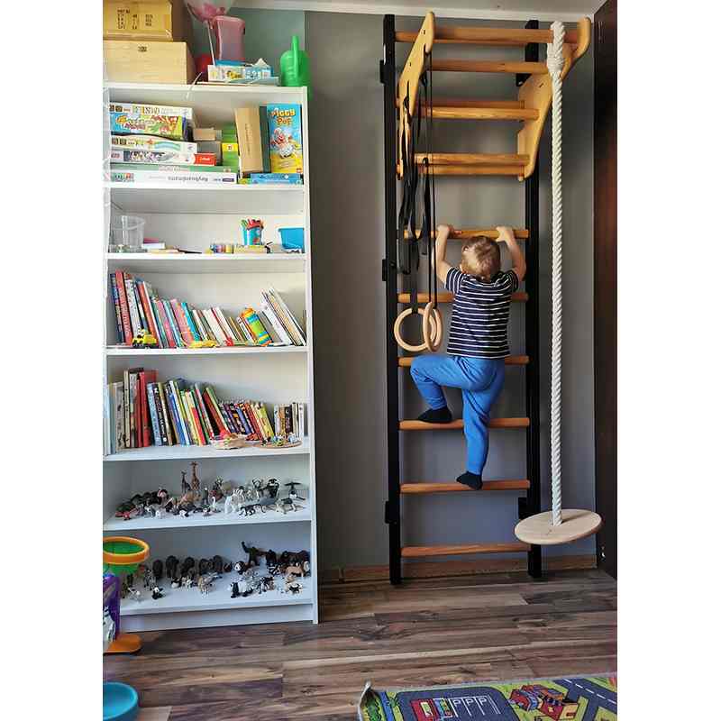 BenchK Wall Bars & Gymnastics Set 711 – child climbing the black nine-rung wall bars beside a bookcase, with wooden pull-up bar, A076 rings and rope swing
