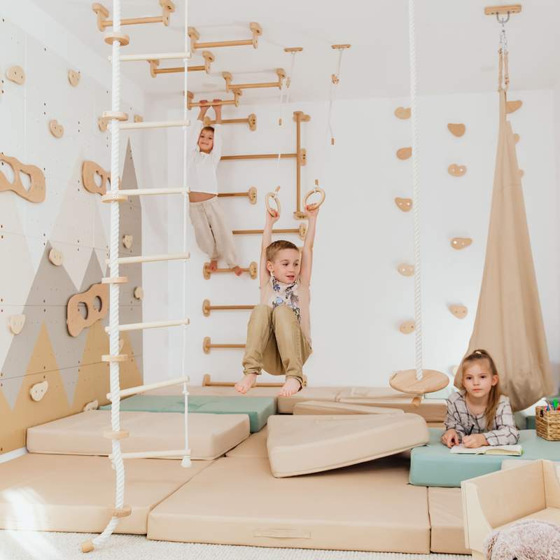Wood and Hearts Climbing Wall Playground – kid hanging from rings beside the mountain wall