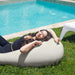 Outdoor Moon Pod – adult reclining on the covered seat on grass beside a pool