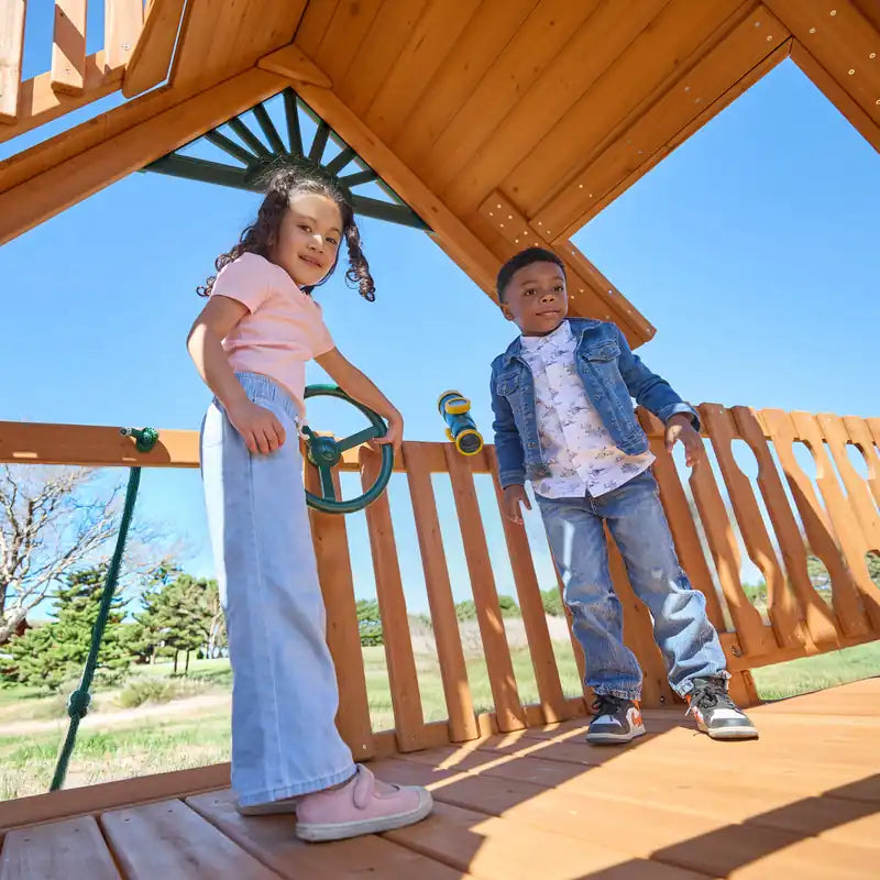 Gorilla Playsets Summerville Deluxe Swing Set – children playing beneath the wooden clubhouse roof