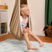 LA SIESTA Joki Teddy Kids Hanging Nest – kid seated beside a playroom bookshelf