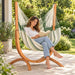 Udine Outdoor Cedar - Weather-Resistant Hammock Chair with FSC® certified Eucalyptus Stand – lifestyle illustration of adult reading in the hammock chair on a patio