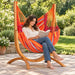 Udine Outdoor Toucan - Weather-Resistant Hammock Chair with FSC® certified Eucalyptus Stand – lifestyle illustration of adult reading in the hammock chair on a patio