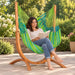 Udine Outdoor Lime - Weather-Resistant Hammock Chair with FSC® certified Eucalyptus Stand – lifestyle illustration of adult reading in the hammock chair on a patio
