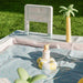 Smol Pool Day Water Table sign, palm trees, umbrellas, and poolside lounge area