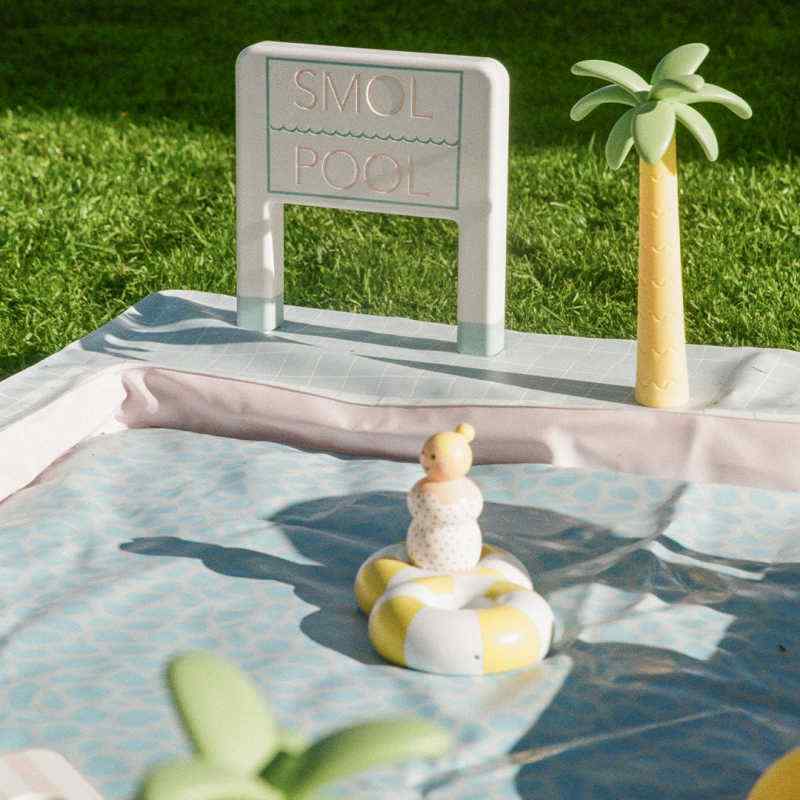 Smol Pool Day Water Table sign, palm trees, umbrellas, and poolside lounge area