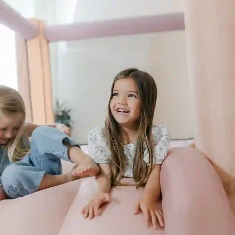 Kid using the slide on the Smol Rainbow Pink Bounce House