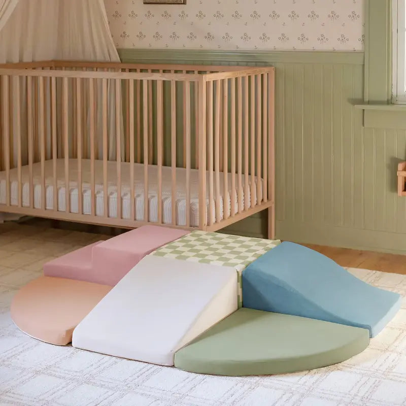 Tiny Land® PlayNest Climbing Blocks - Morandi – Morandi foam climbing blocks arranged on a rug beside a crib