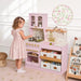 Tiny Land® Wooden Play Kitchen with Storage for Creative Toddlers – Child at the Sakura Pink kitchen with a floral-panel detail